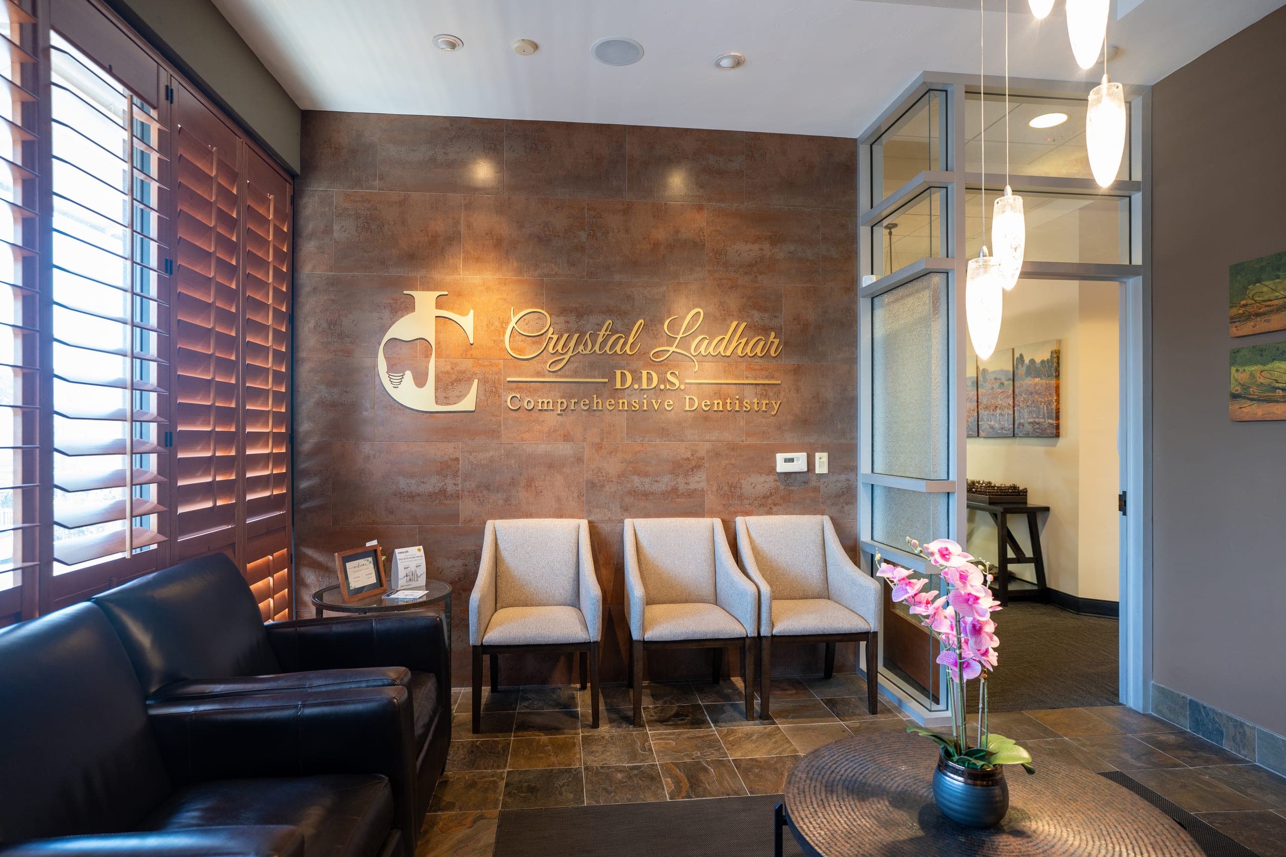 The practice reception, the Crystal Ladhar DDS name in gold lettering on a copper-toned tile wall above three cream armchairs