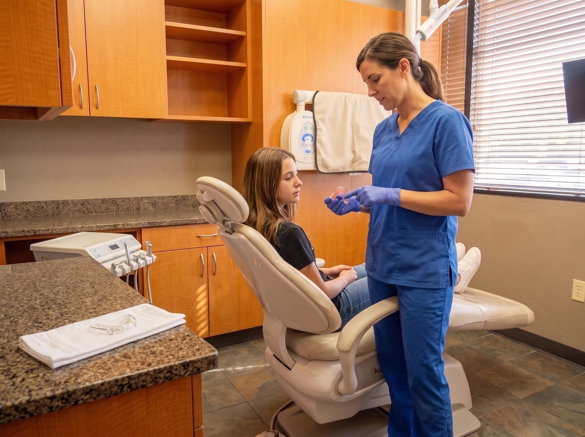A clinician showing a wire and acrylic retainer to a young patient in the treatment chair