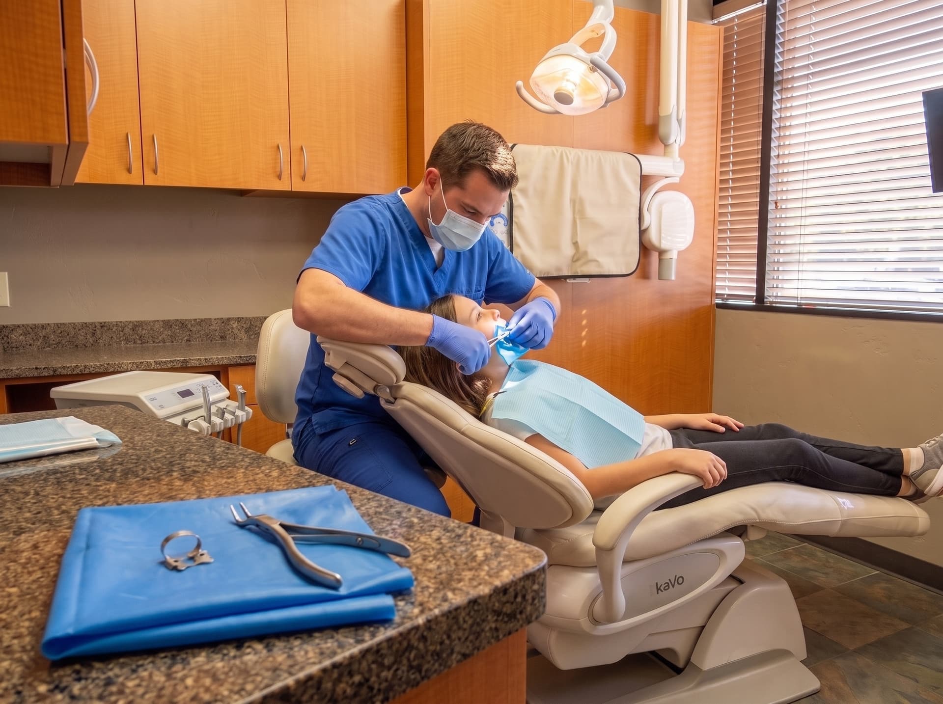 A clinician placing a blue rubber dam for a child reclined in the treatment chair