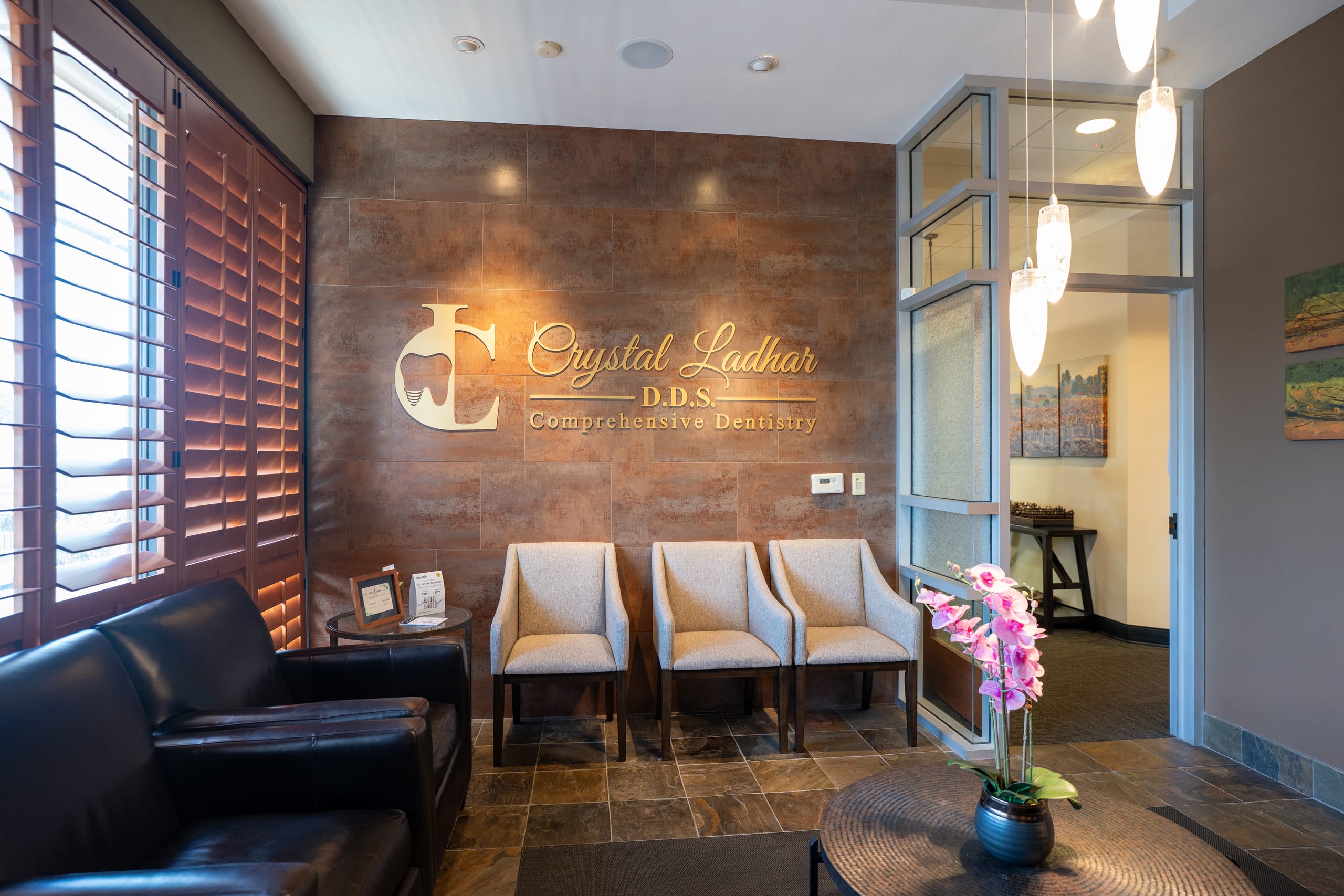 The practice reception, the Crystal Ladhar DDS name in gold lettering on a copper-toned tile wall above three cream armchairs
