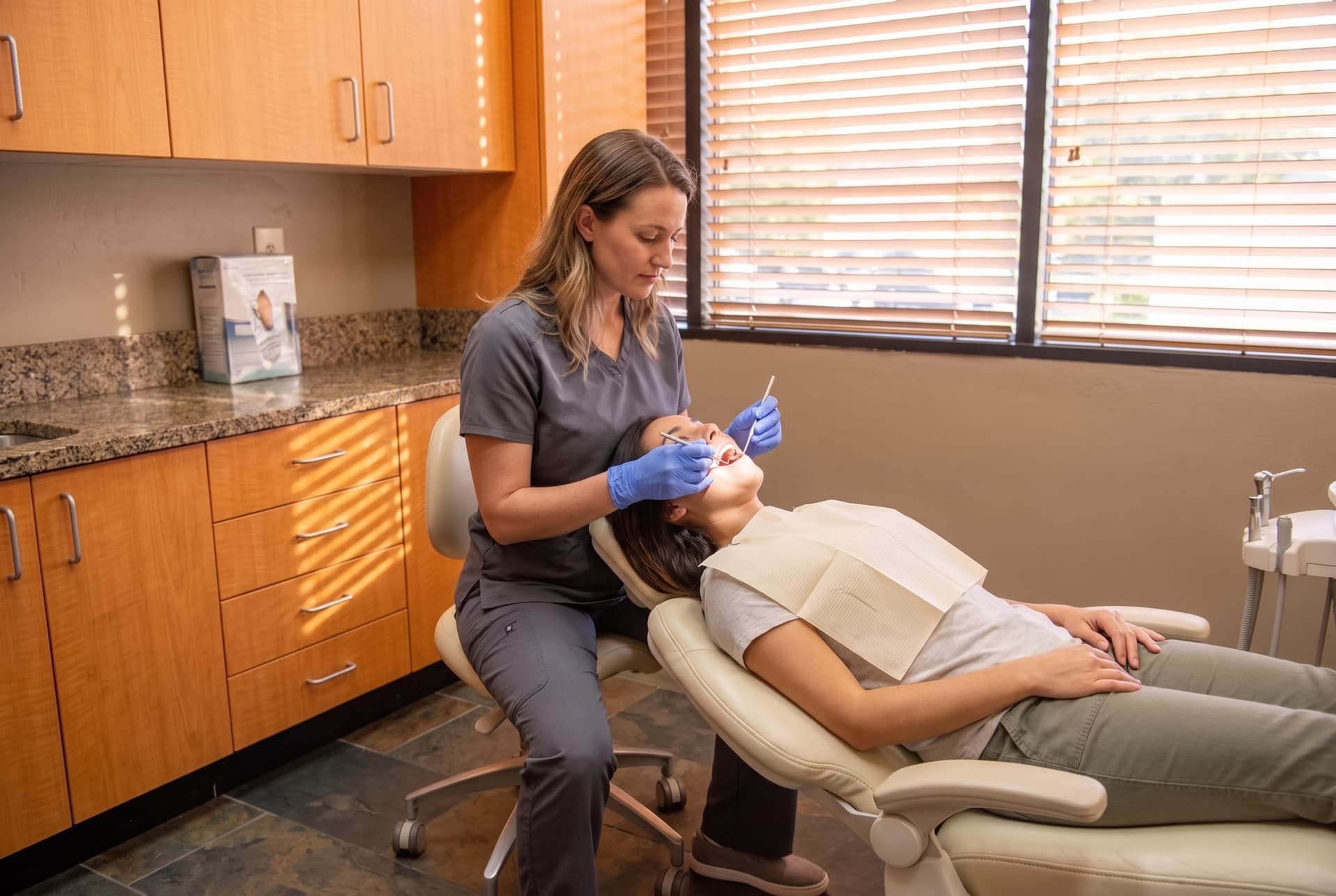 A hygienist working chairside on a reclined patient with a dental mirror and explorer probe