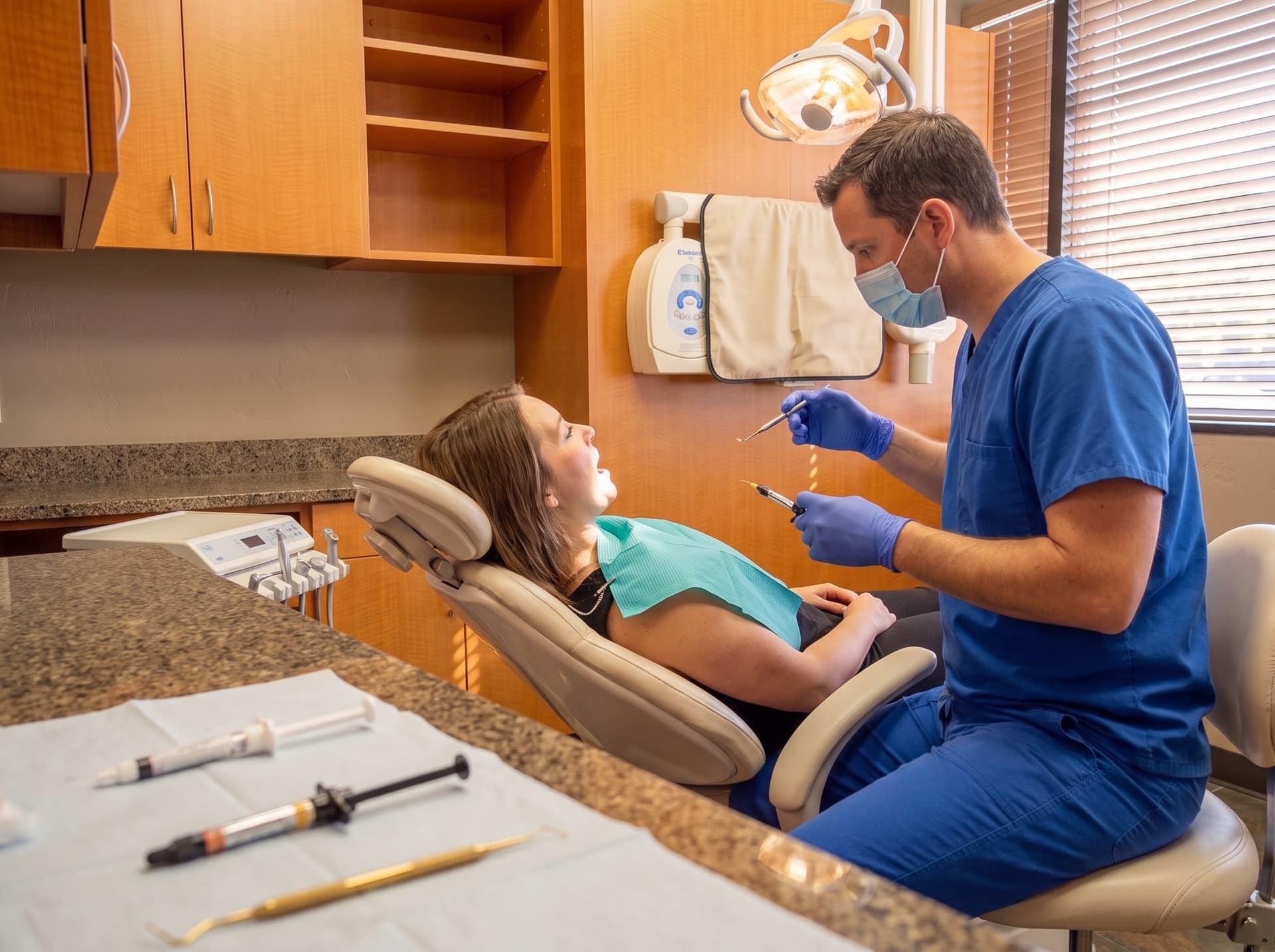 A clinician placing a filling for a reclined patient, composite syringes on the sterile field in the foreground